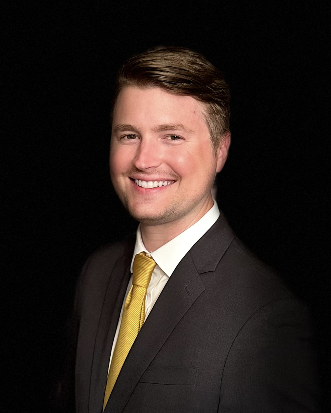Man in blue suit and patterned tie, smiling in an office setting.