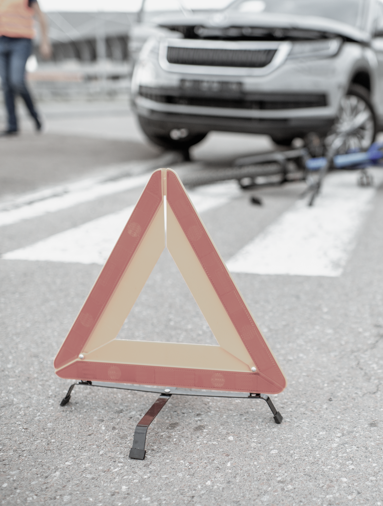 A warning triangle is sitting on the side of the road in front of a car accident.