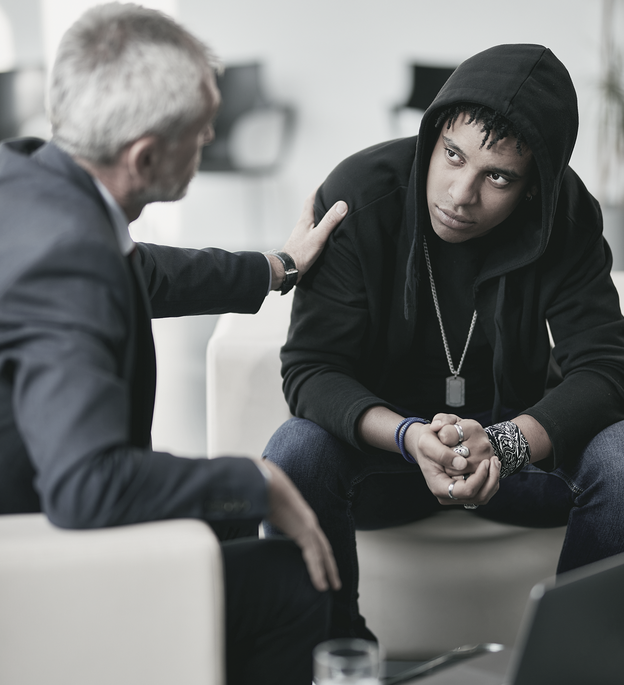 A man in a suit is comforting a man in a black hoodie