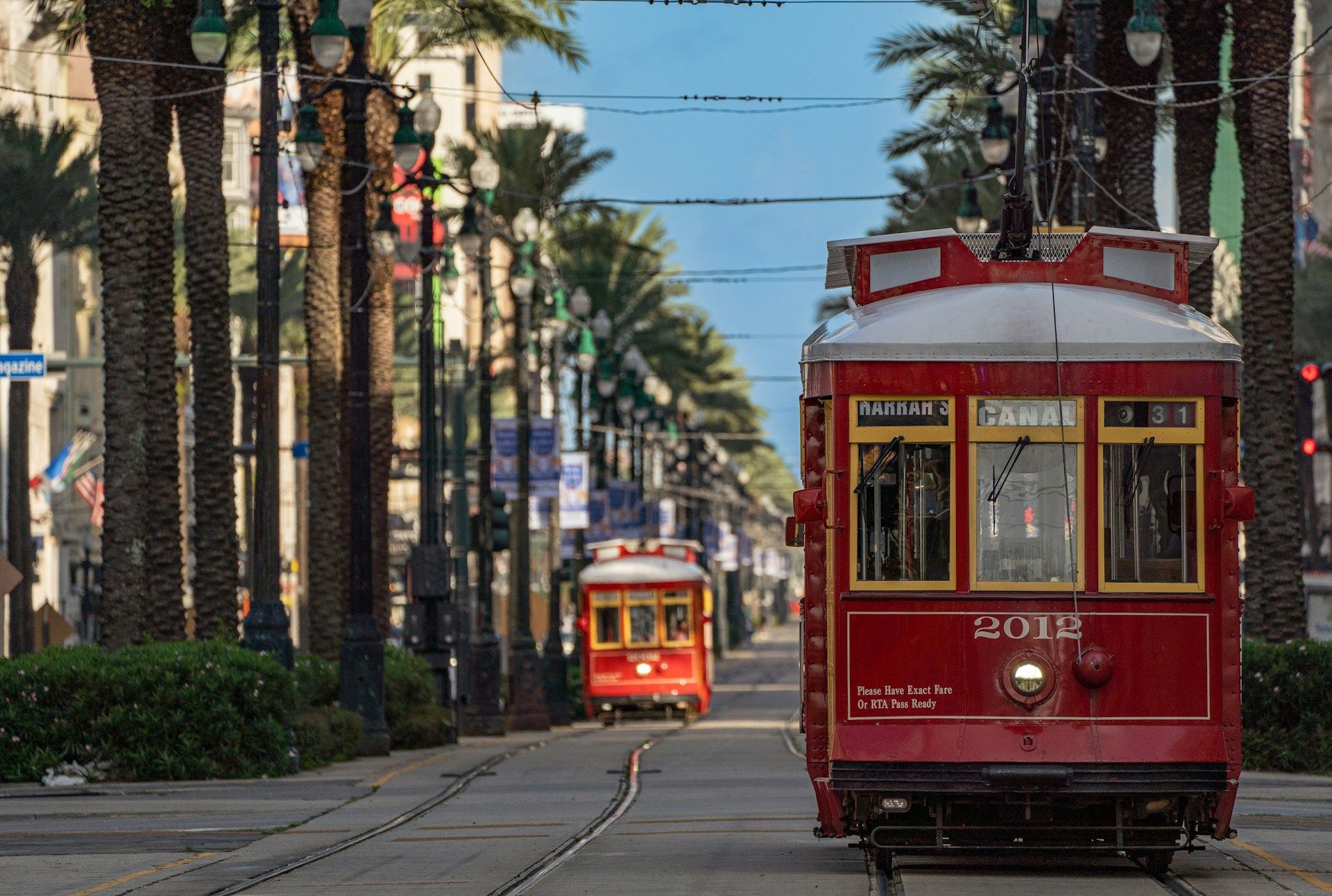 Two red streetcars travel down St. Charles Avenue in New Orleans, lined with palm trees.
