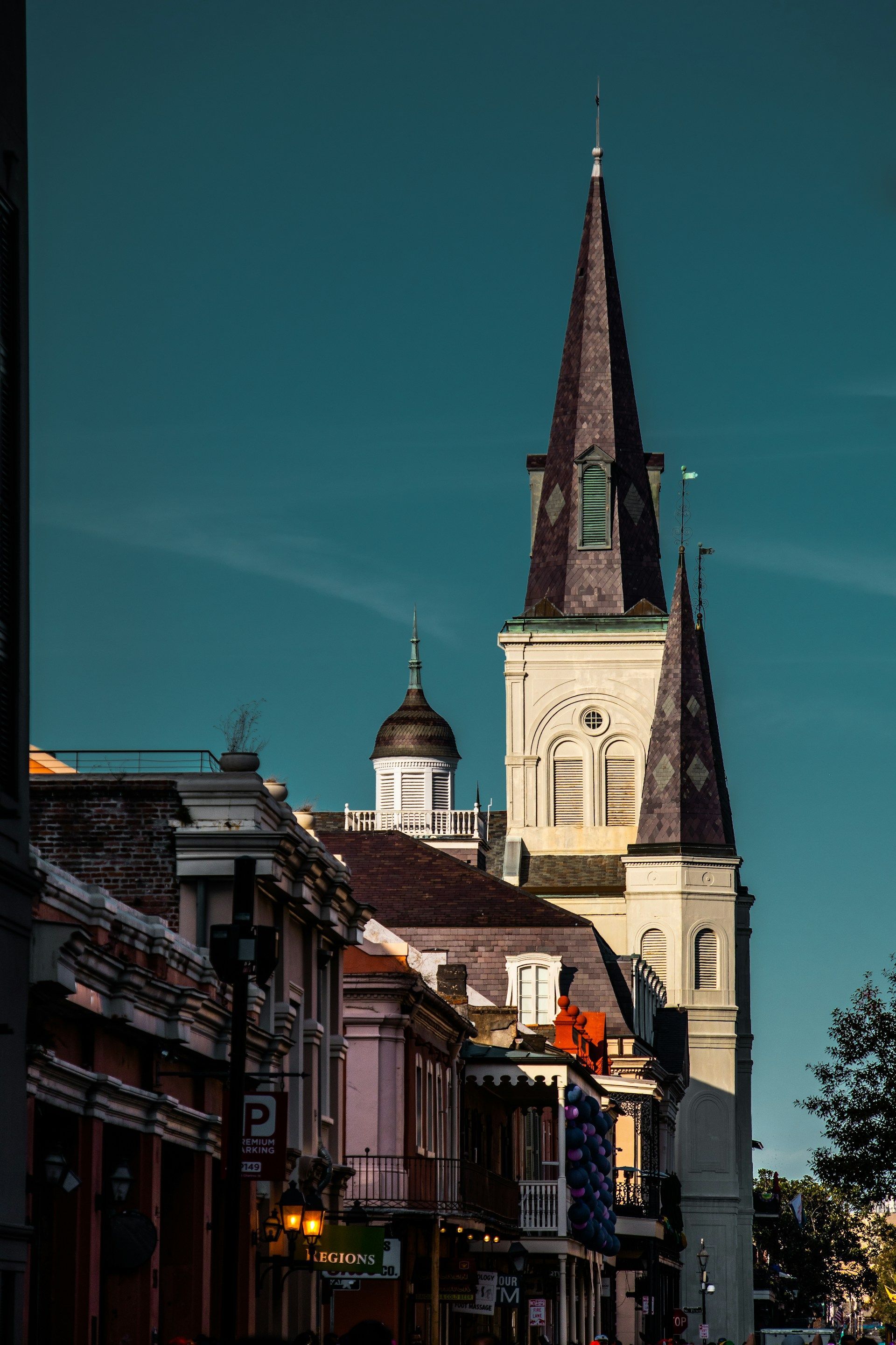 Church steeple rising above buildings in New Orleans, with a teal sky.