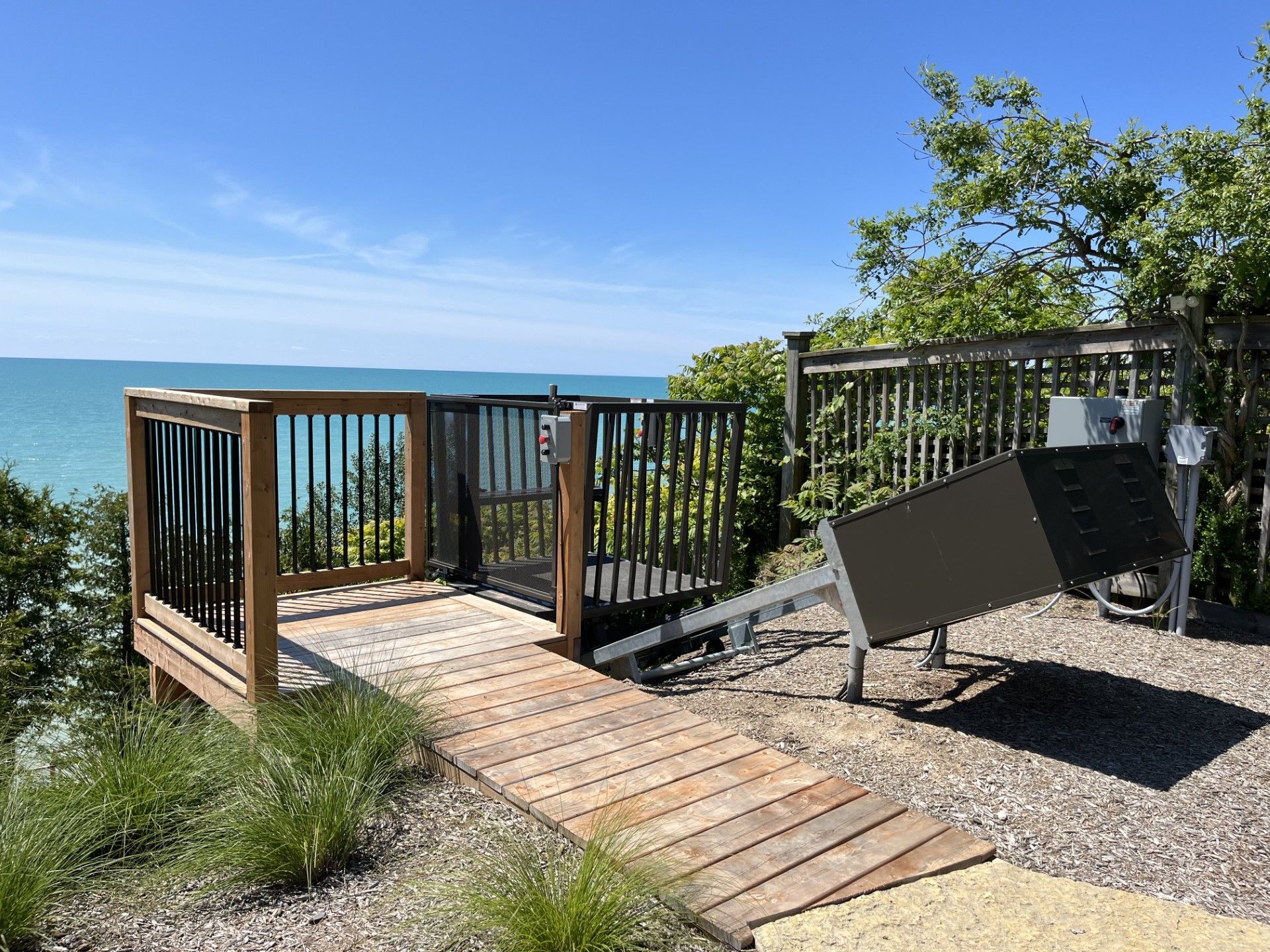 Wooden ramp leading to an accessible viewing platform overlooking a turquoise body of water under a blue sky.