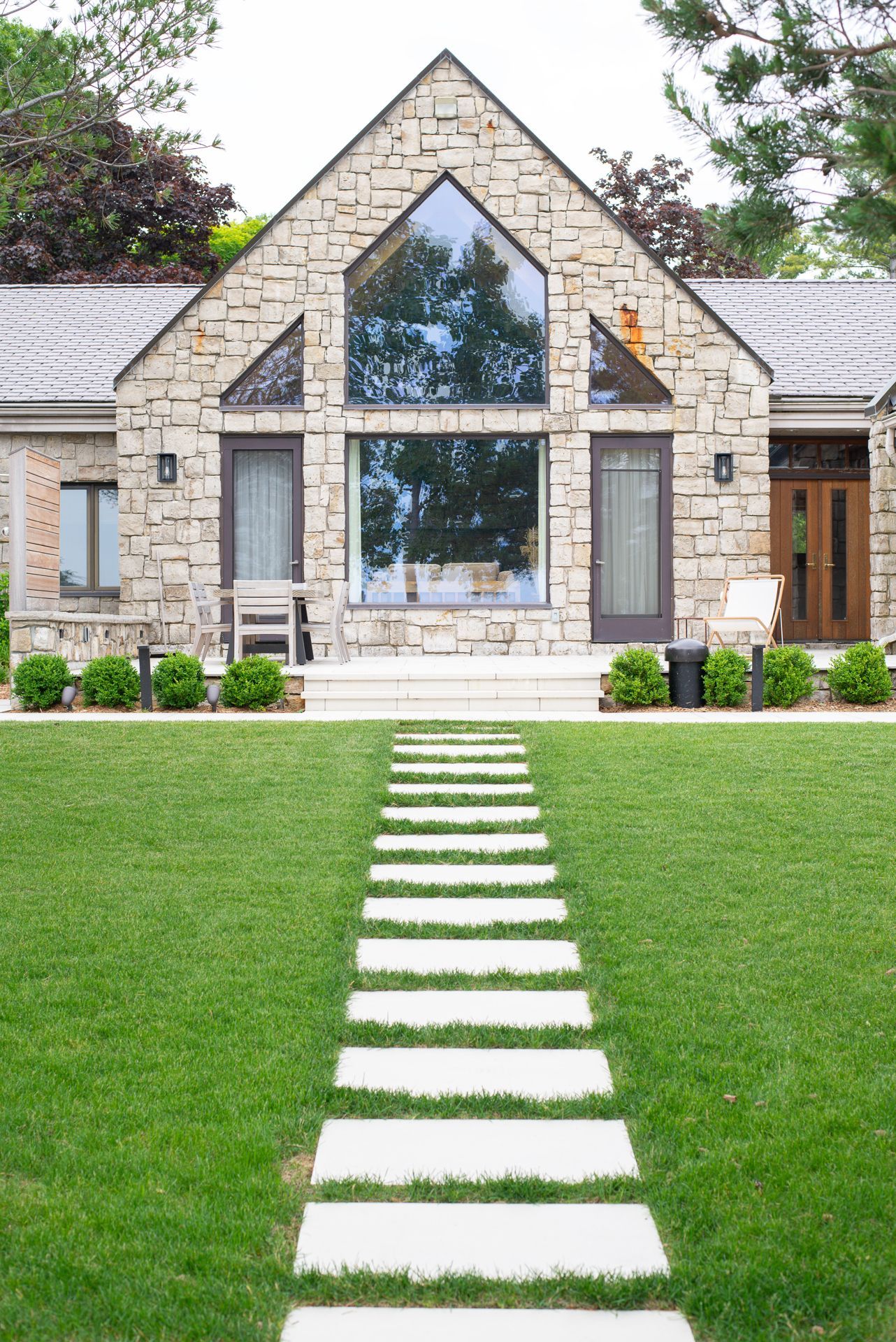 Stone house with a pathway of square pavers through green grass leading to the entrance.