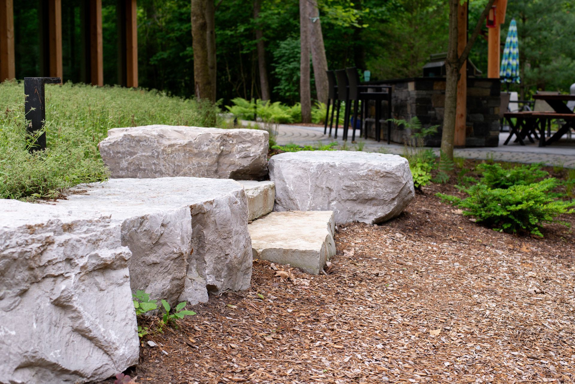 Large, light-colored stone steps leading through a brown gravel bed, with trees and a building in the background.