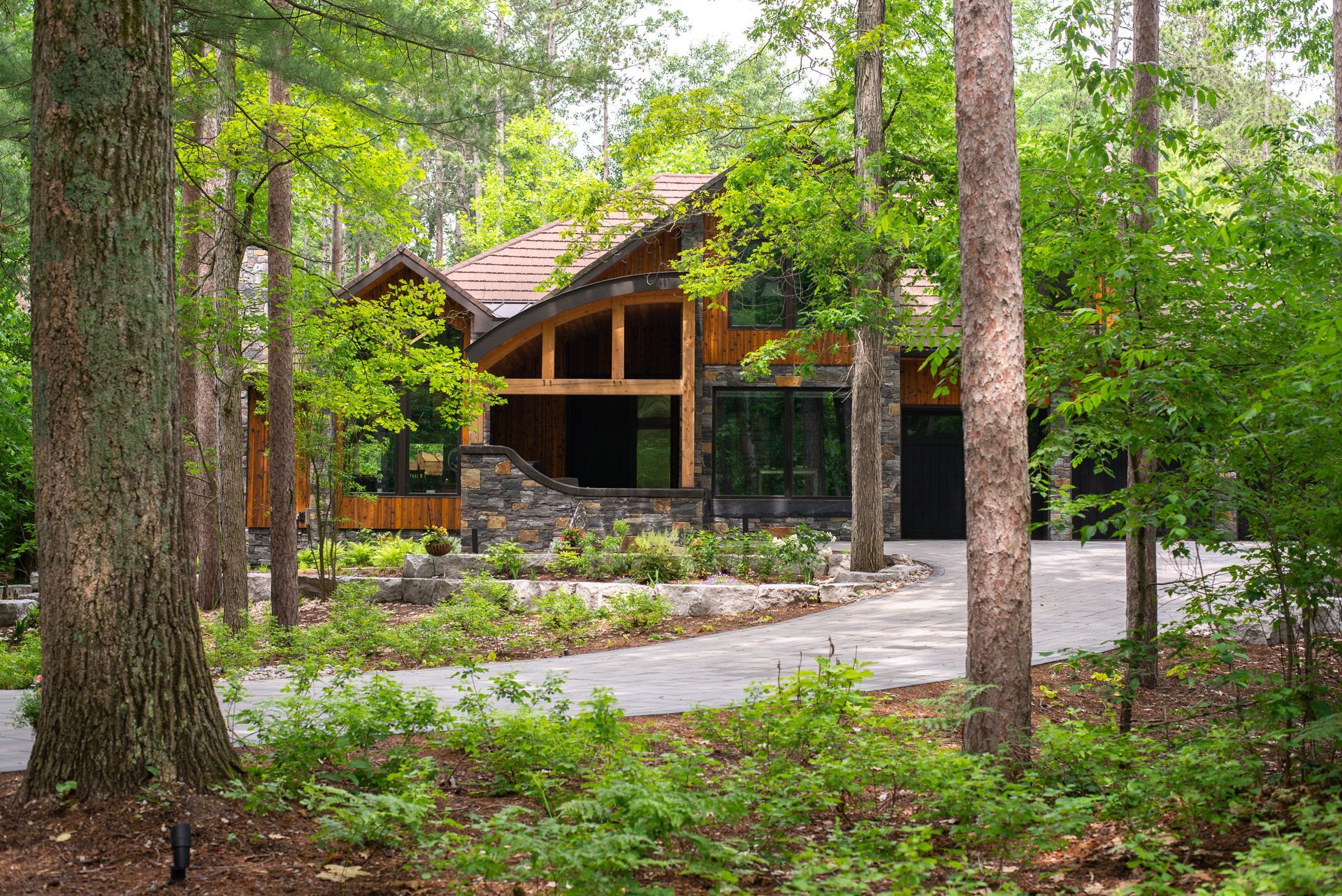 house nestled in a forest with a stone entryway and gravel driveway designed by Cobble Design