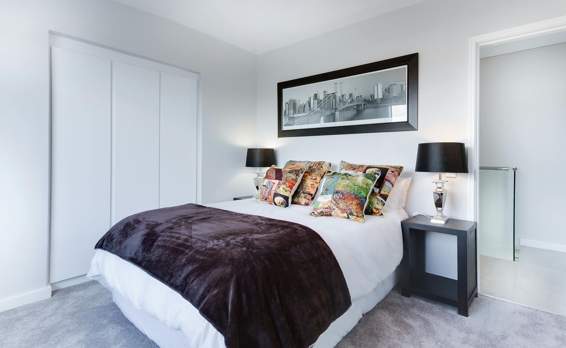 Une chambre avec un lit, une table de chevet, des lampes et un tableau sur le mur au-dessus du lit.