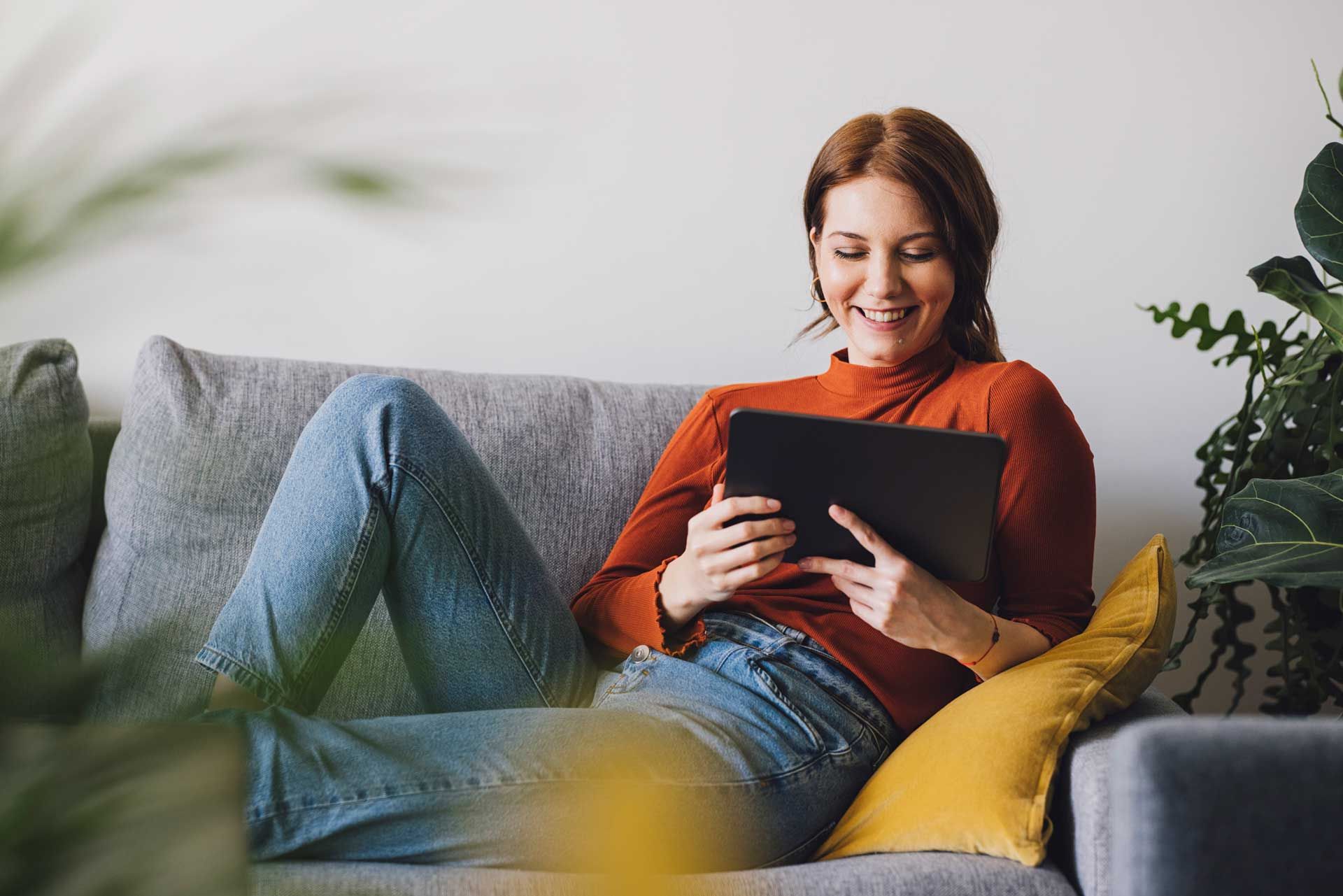 A woman is sitting on a couch using a tablet computer.