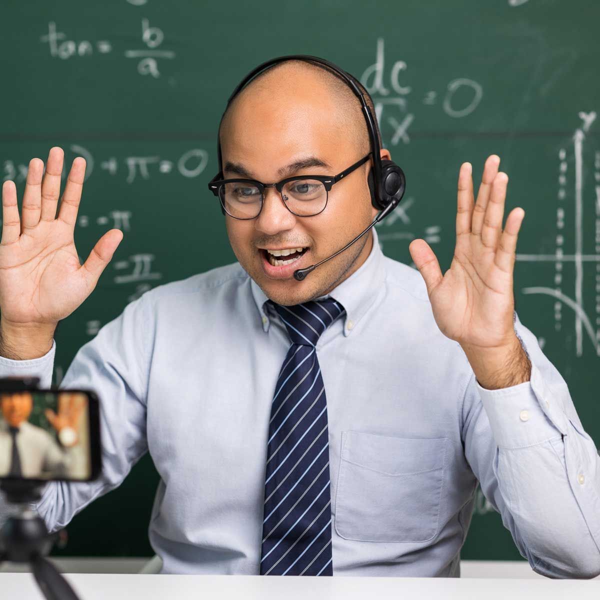 A man wearing headphones and a tie is sitting in front of a blackboard