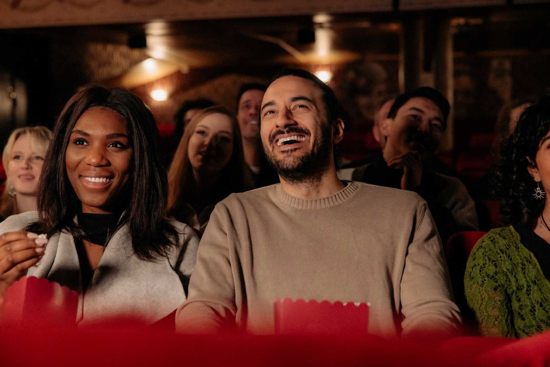 A man and a woman are laughing while watching a movie in a theater.