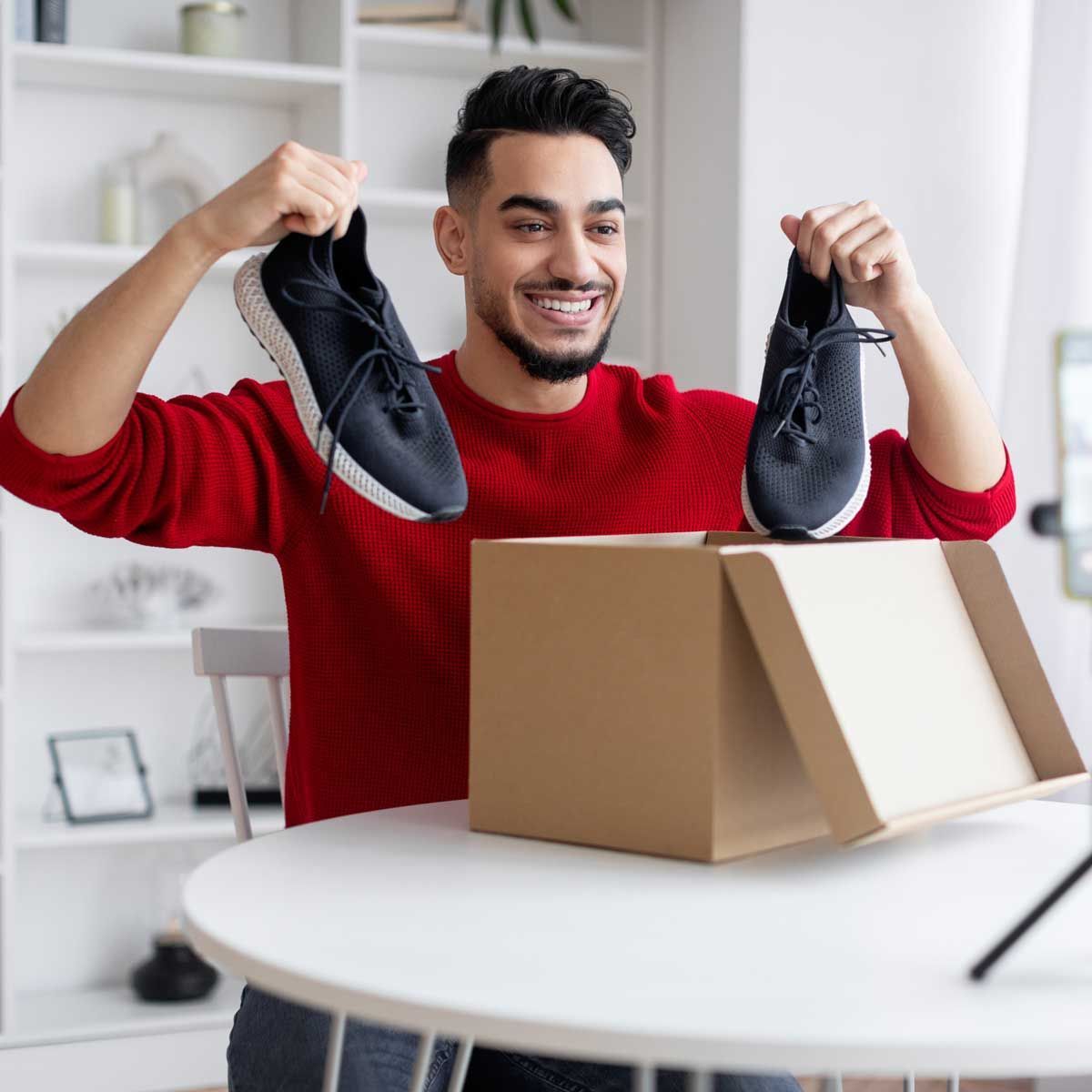 A man in a red sweater is holding a pair of shoes over a cardboard box