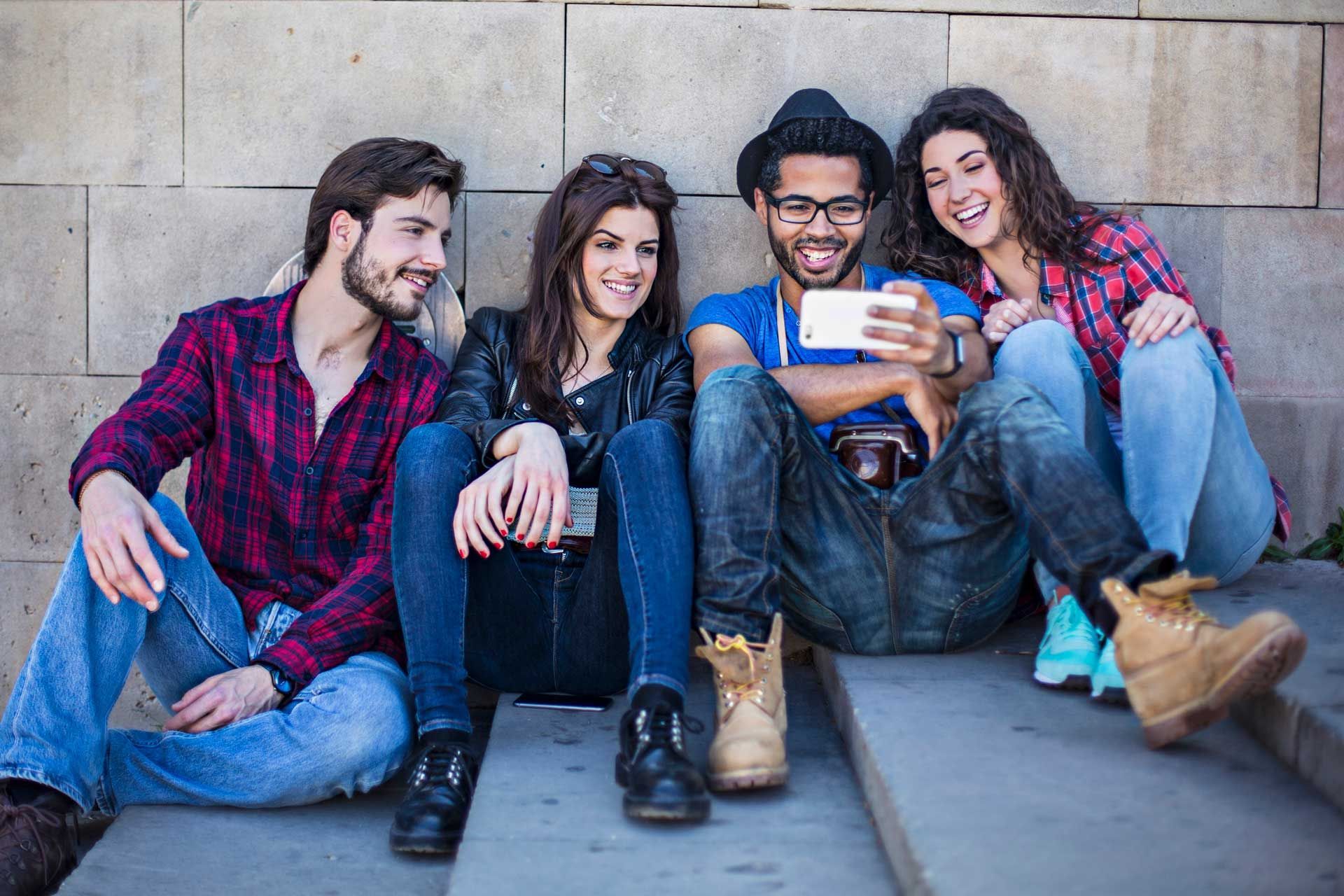 A group of young people are sitting on steps taking a selfie with a cell phone.