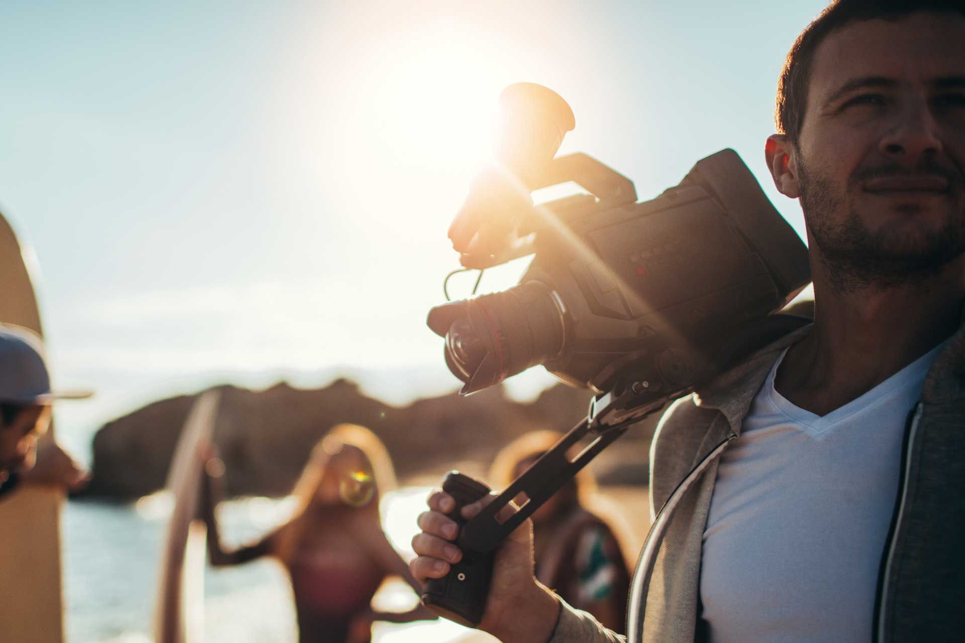 A man is carrying a camera on his shoulder on the beach.