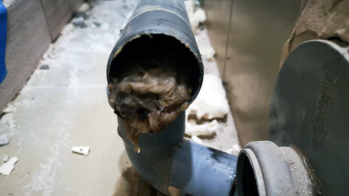 Blocked sewer pipe filled with brown and gray debris.