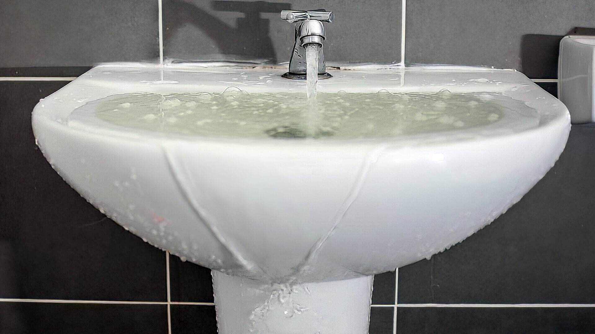 White bathroom sink overflowing with water.