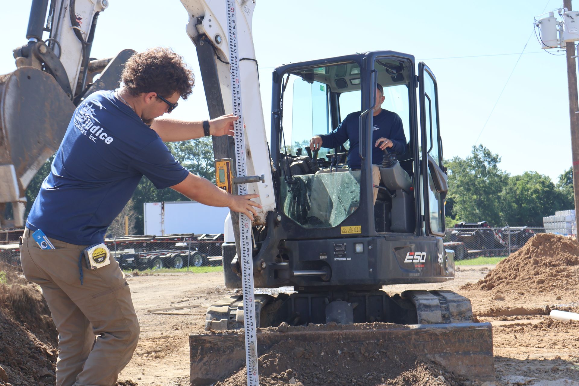 Person using a leveling rod near a mini-excavator at a construction site.