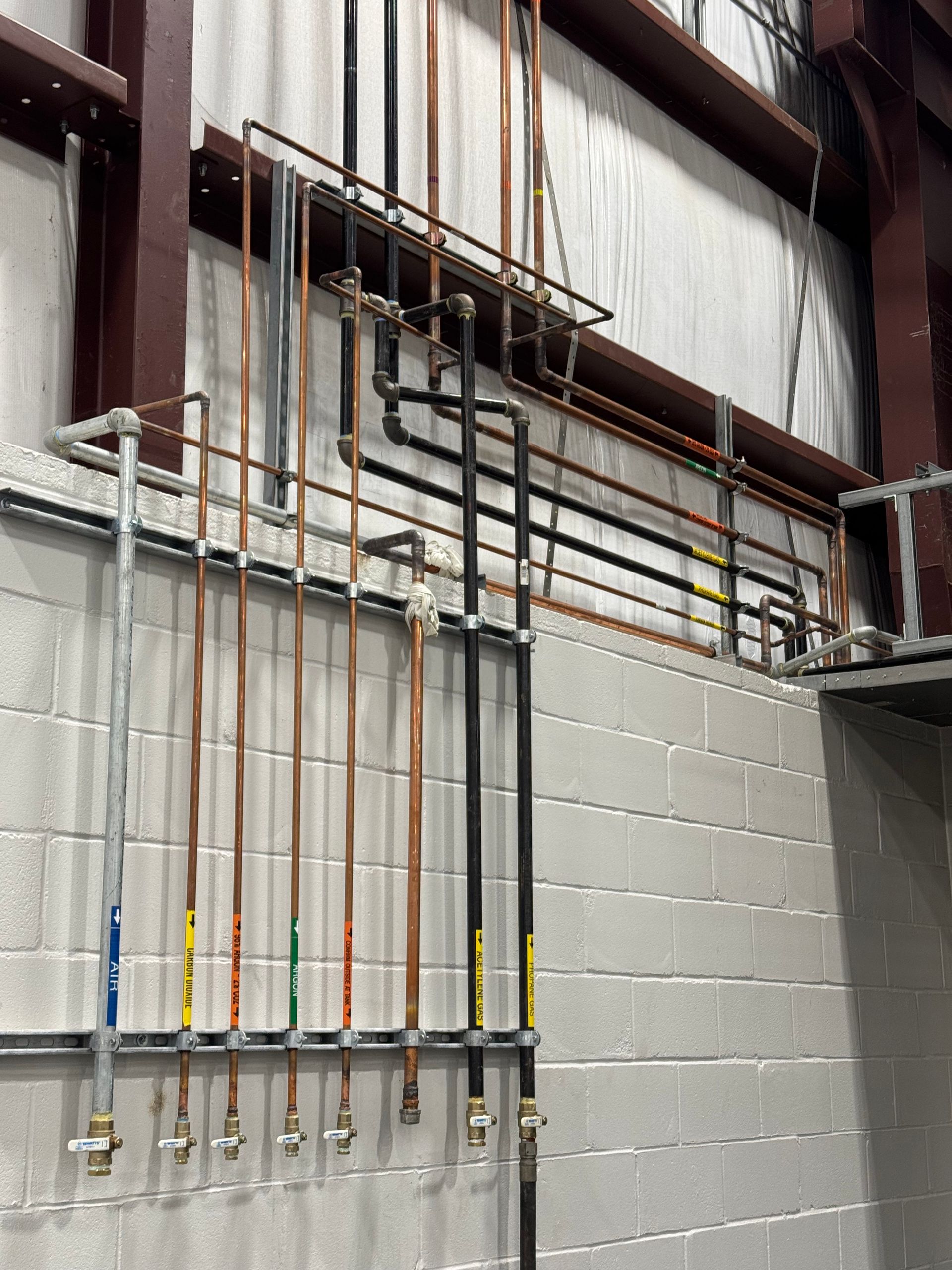 Pipes of various colors, including copper and black, mounted on a brick wall with fittings.