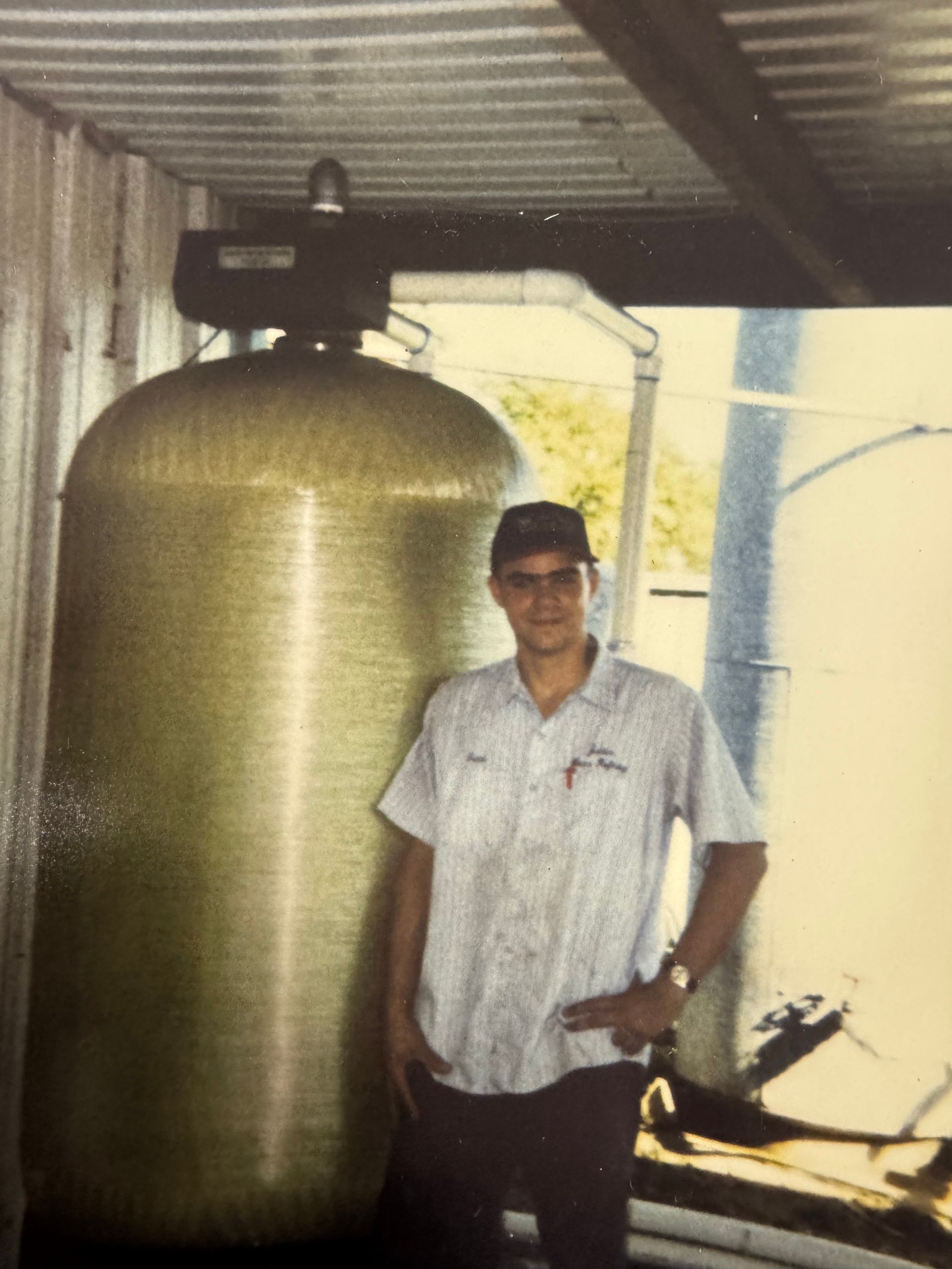 Man in uniform stands next to a large water filtration system, in an outdoor setting.