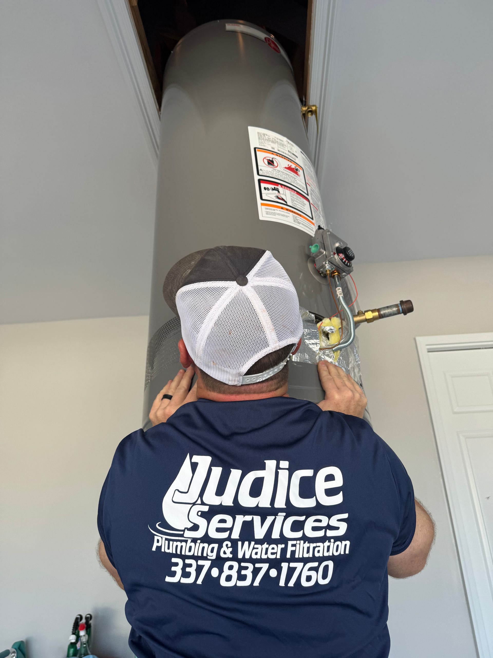 Plumber installing a water heater, working overhead in a utility space.