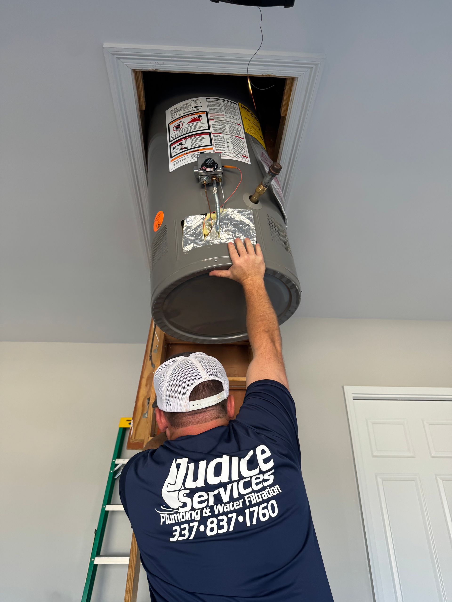 A plumber removes a water heater from an attic. The water heater is gray.