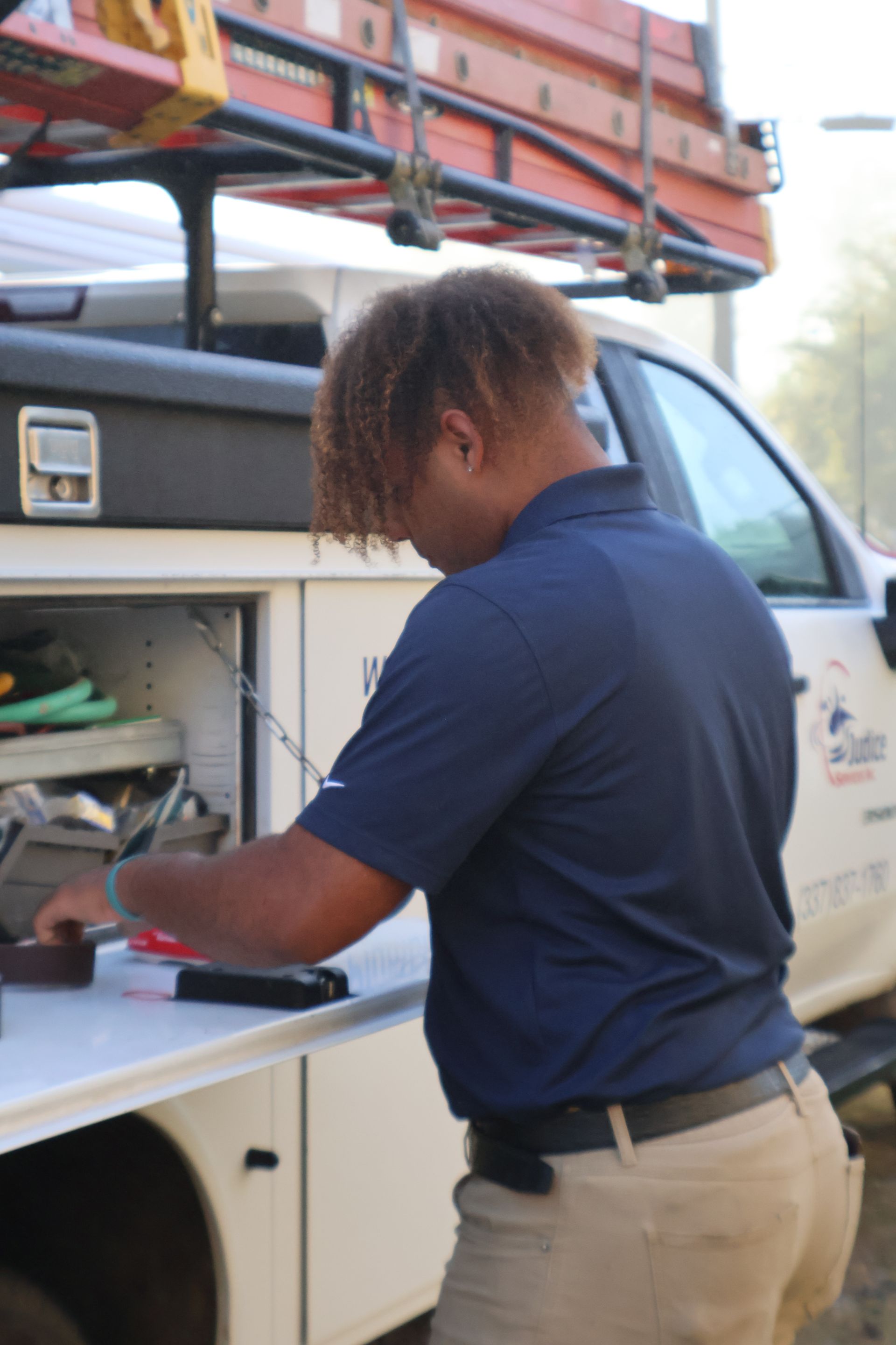 Person in blue shirt and khaki pants, working at a utility truck.