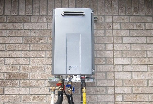 A person in a hard hat inspects a white boiler on a wall. Plumbing and a fuse box are visible.