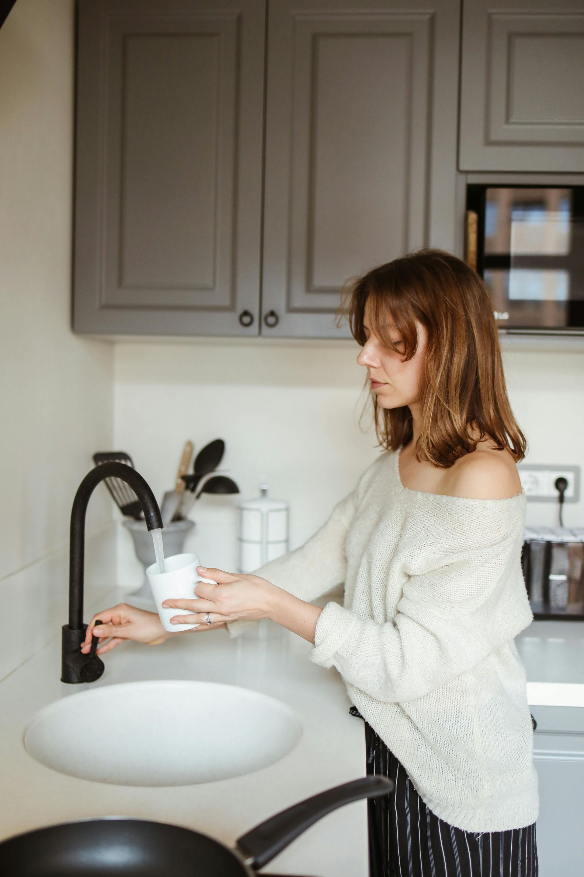 Woman filling a glass with water from a black faucet in a gray kitchen.