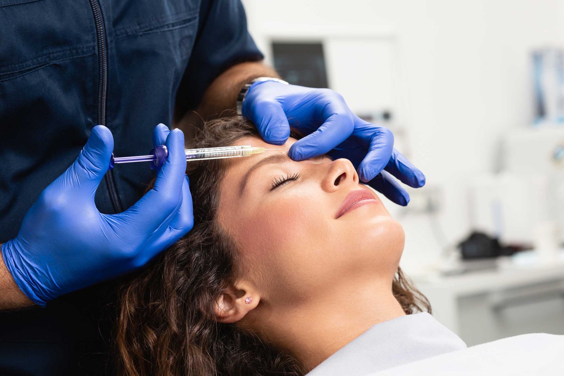 Close-up of a beautician expert's hands injecting Botox treatment in a female's forehead.