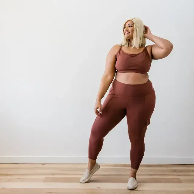 A woman in a crop top and leggings is standing on a wooden floor.