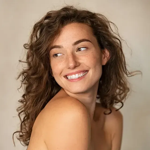 A woman with curly hair is smiling and looking over her shoulder.
