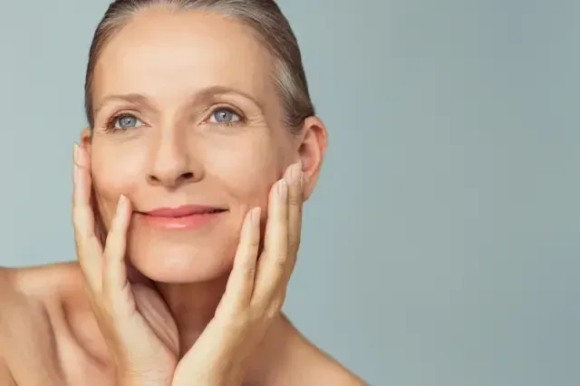 A woman is touching her face with her hands and smiling.