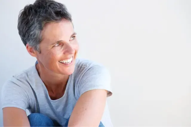 A woman is sitting on the floor with her legs crossed and smiling.