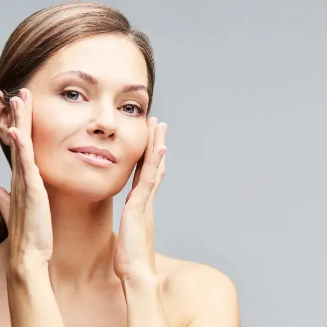 A woman is touching her face with her hands and smiling.