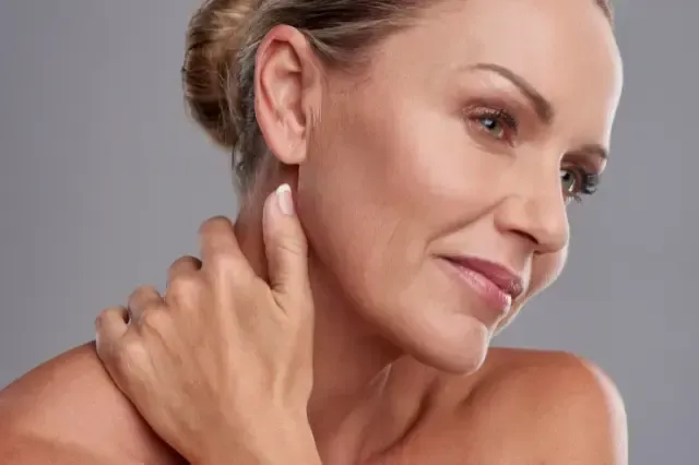 A woman is touching her neck with her hand and smiling.