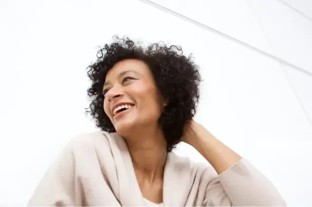 A woman with curly hair is smiling and looking up.