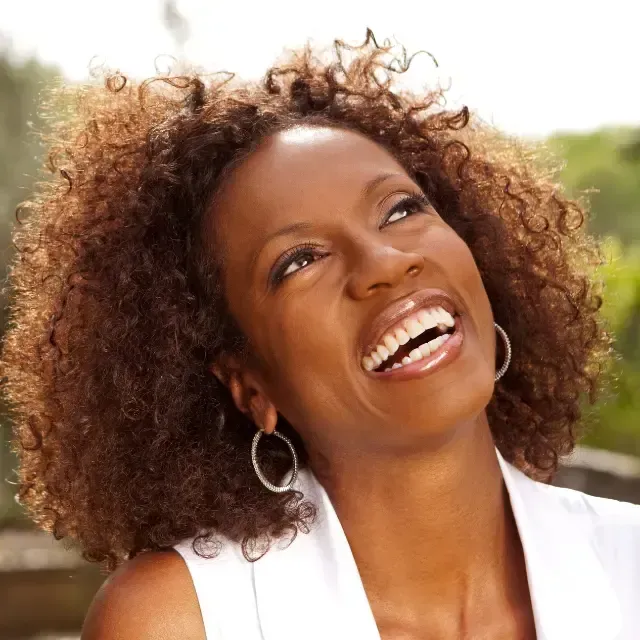 A woman with curly hair is smiling and wearing hoop earrings