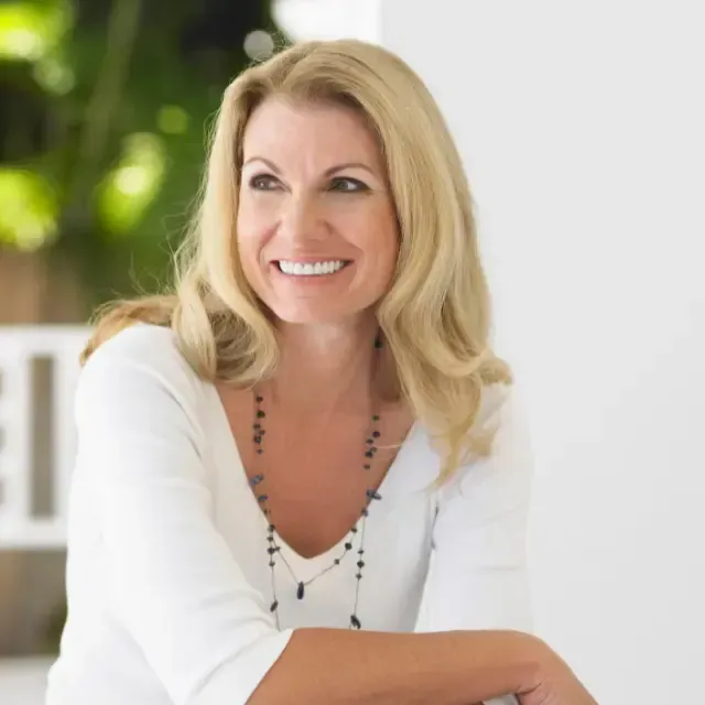 A woman in a white shirt and necklace is smiling