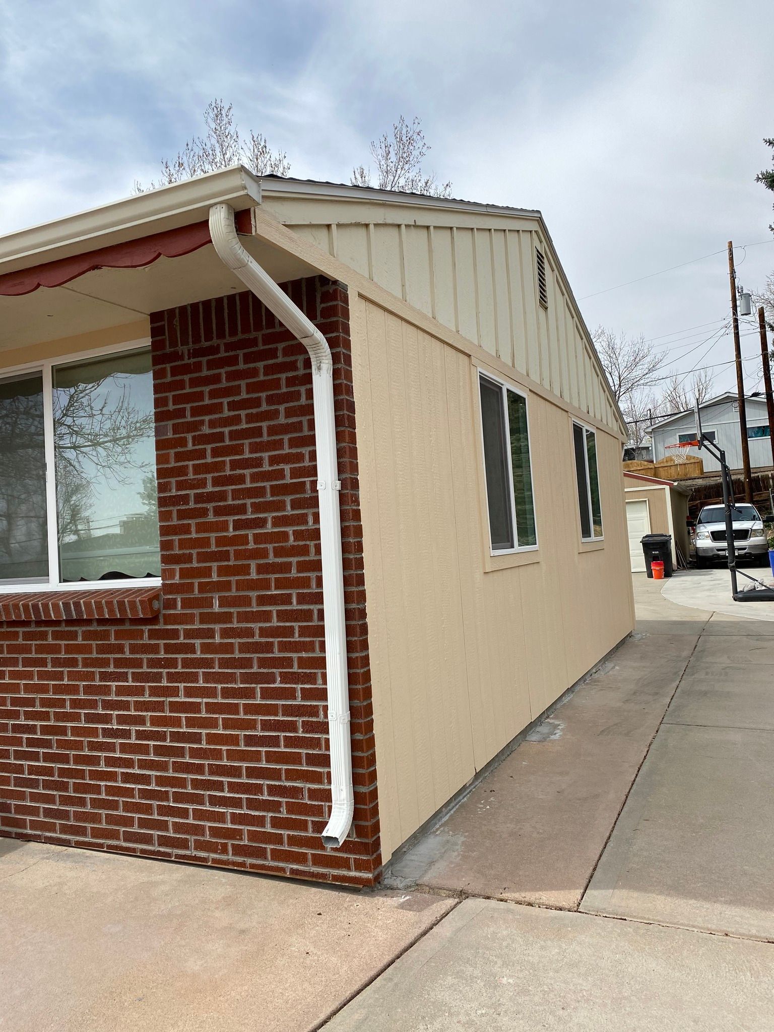 A side view of a house exterior featuring a brick front, tan stucco walls, vertical wood siding, and a white downspout.