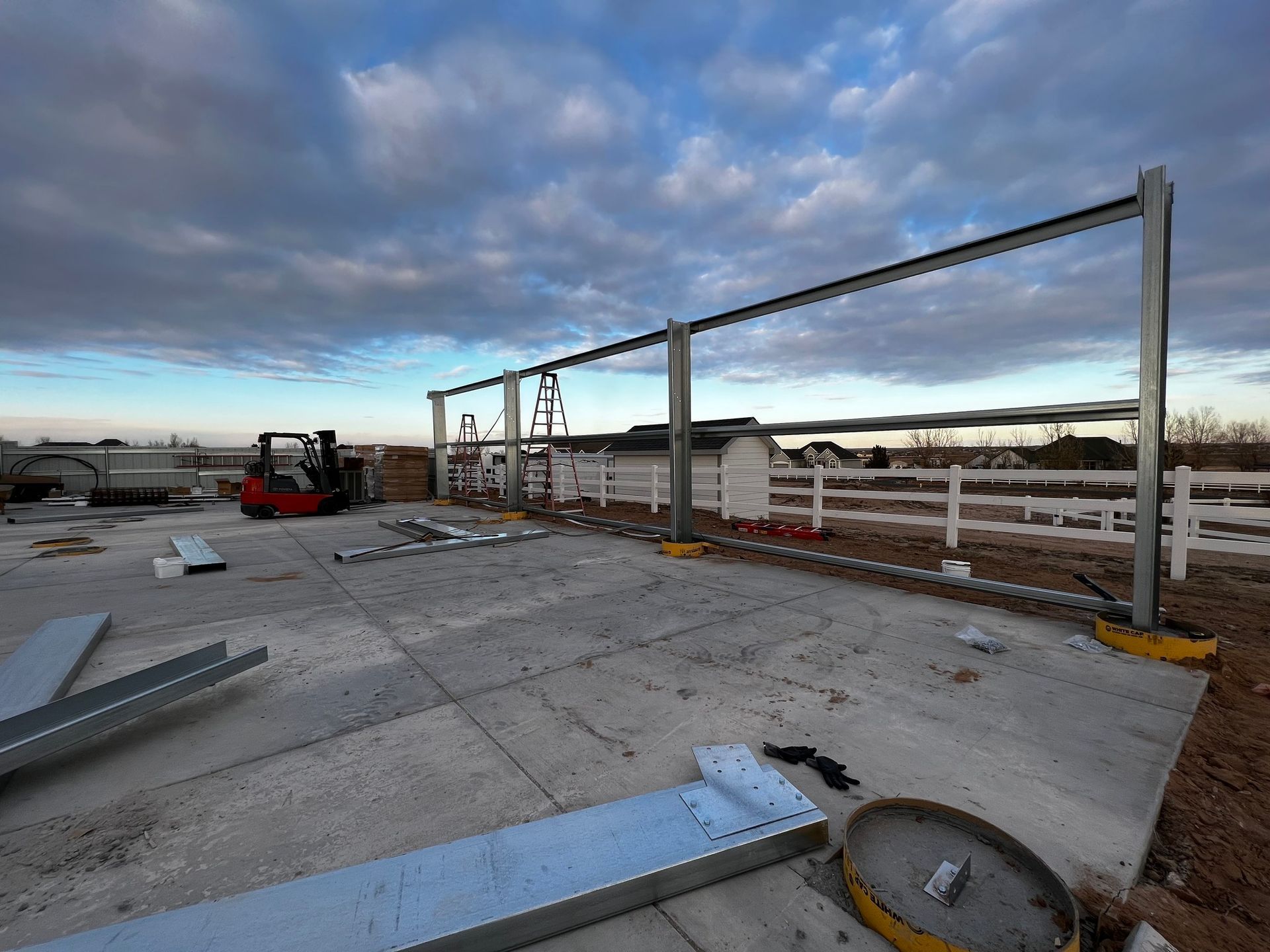 Steel vertical beams and horizontal girts being assembled for a building frame on a concrete slab at sunset.