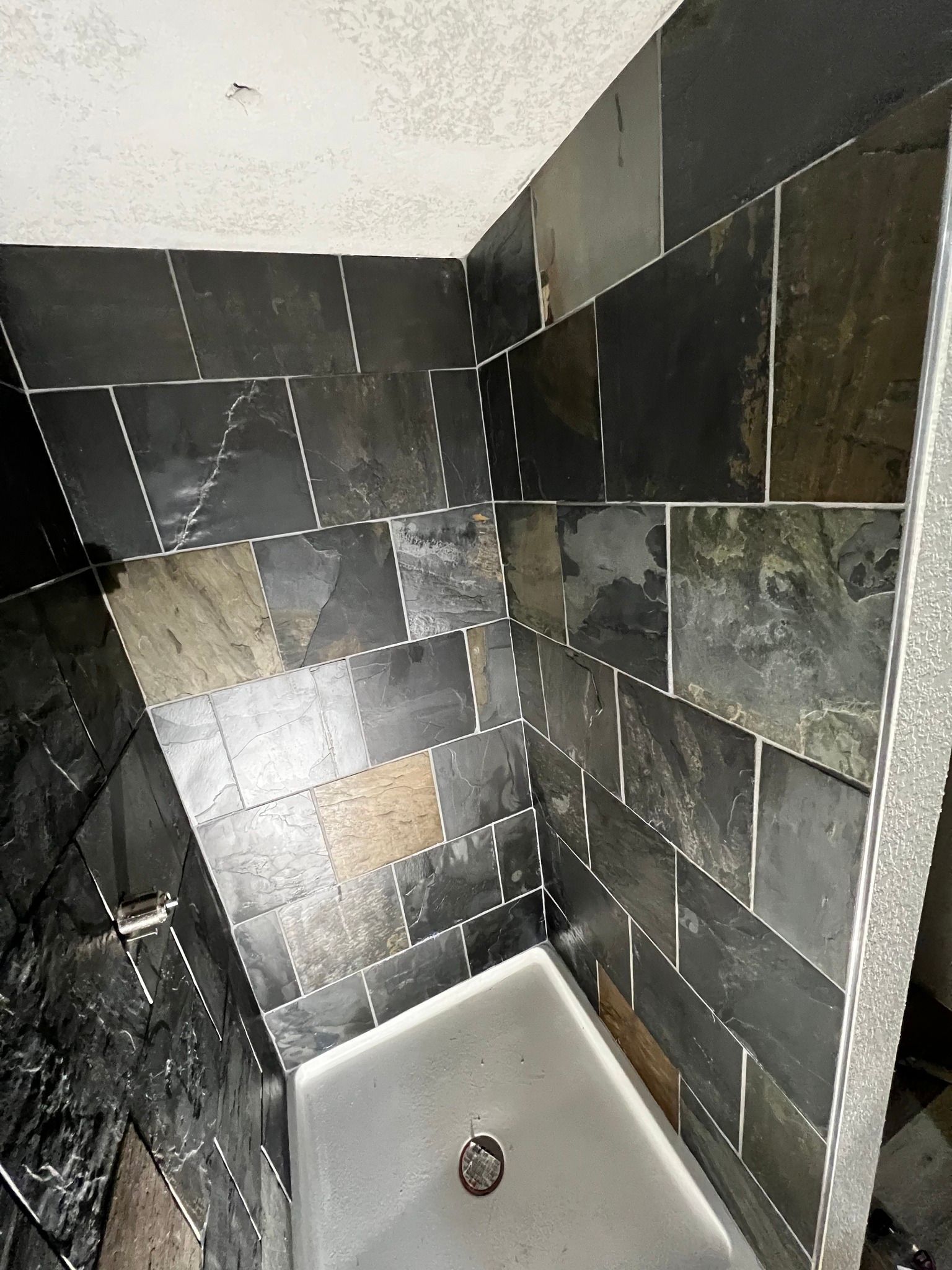 A shower stall with dark, multi-toned slate tile walls and a white rectangular shower pan.