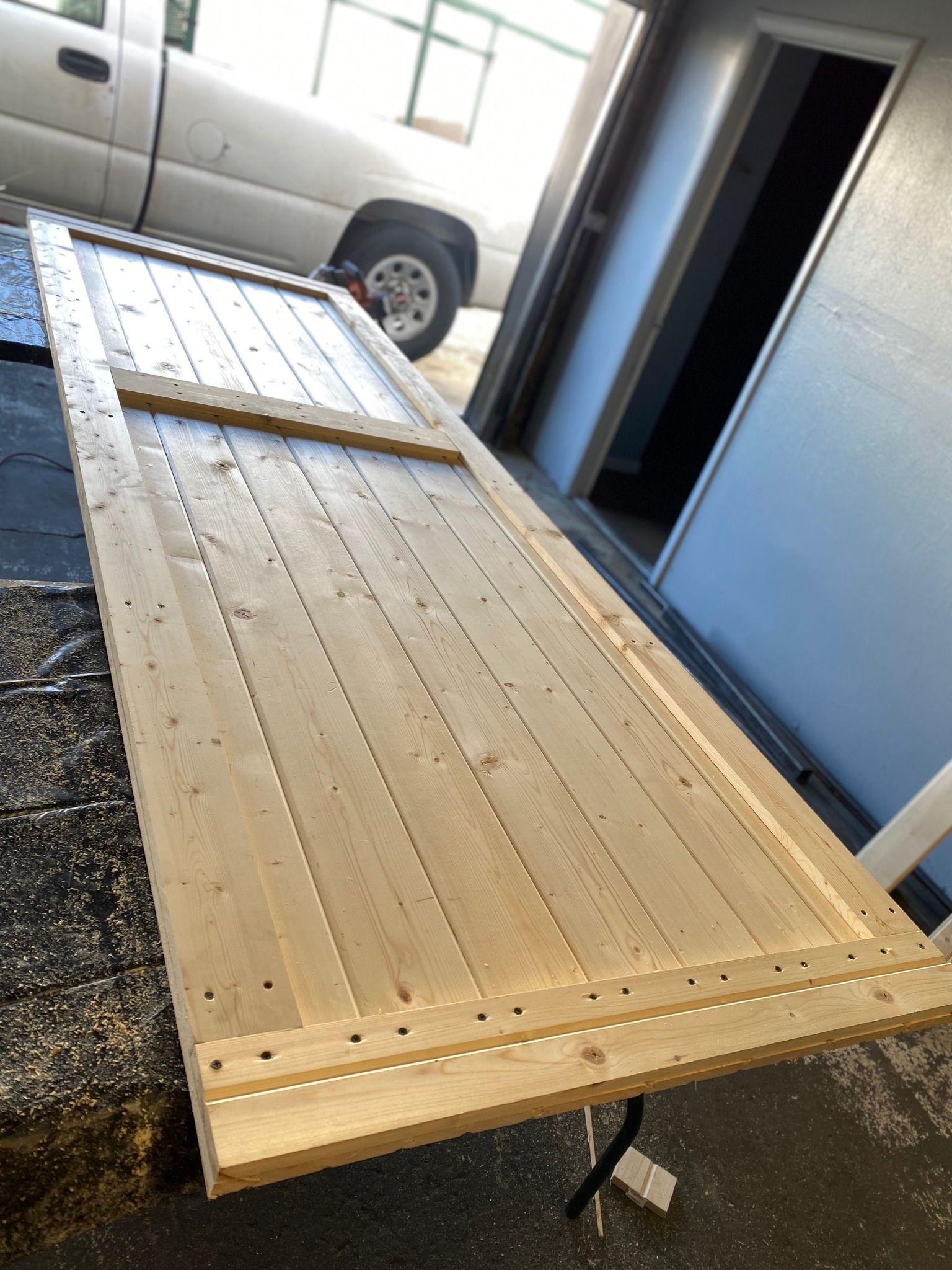 A wooden gate or door under construction, featuring vertical planks framed by horizontal beams in a garage setting.
