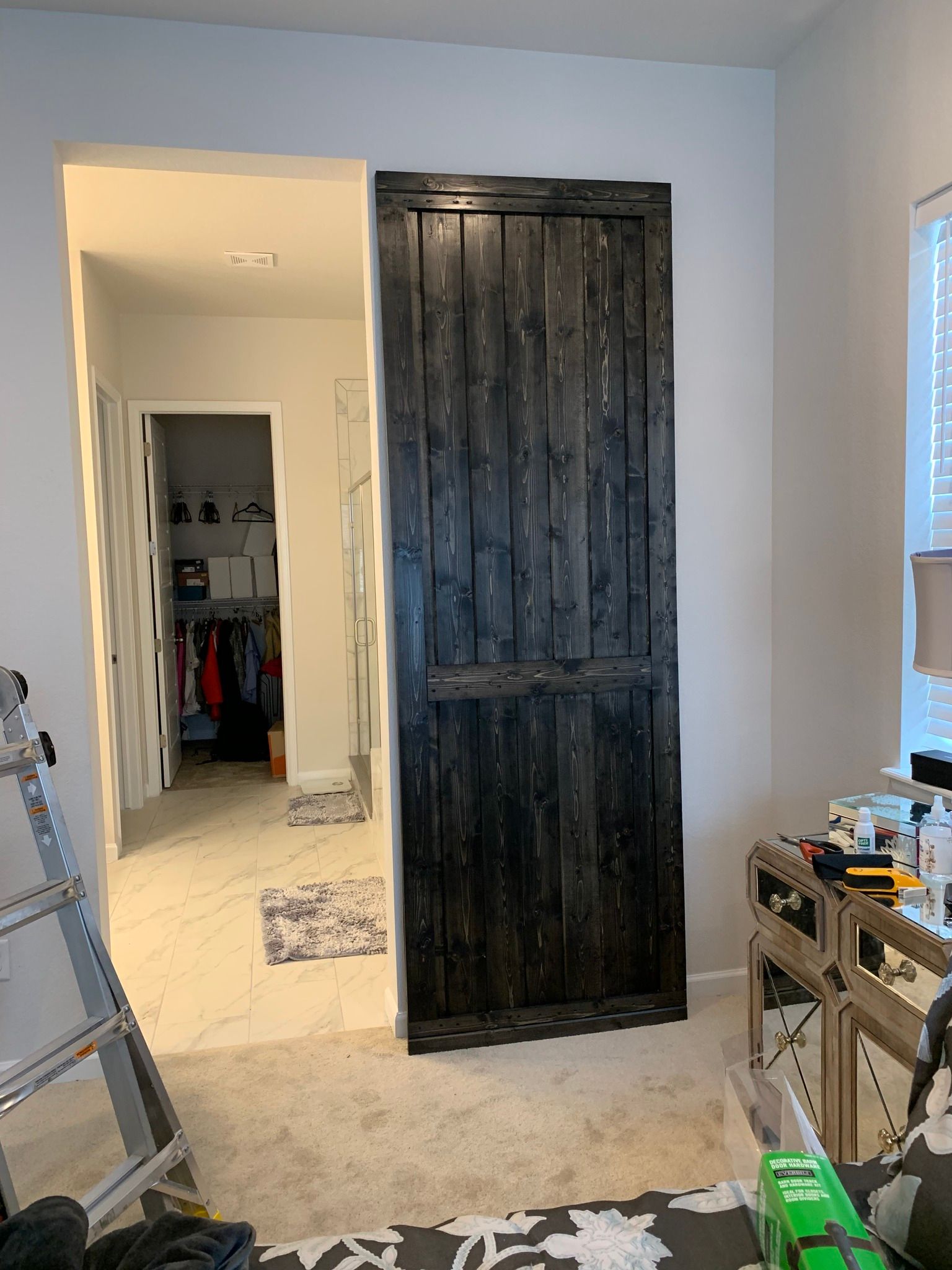 A rustic, black-stained vertical-plank sliding door partially covering the entrance to a room with white marble floors.