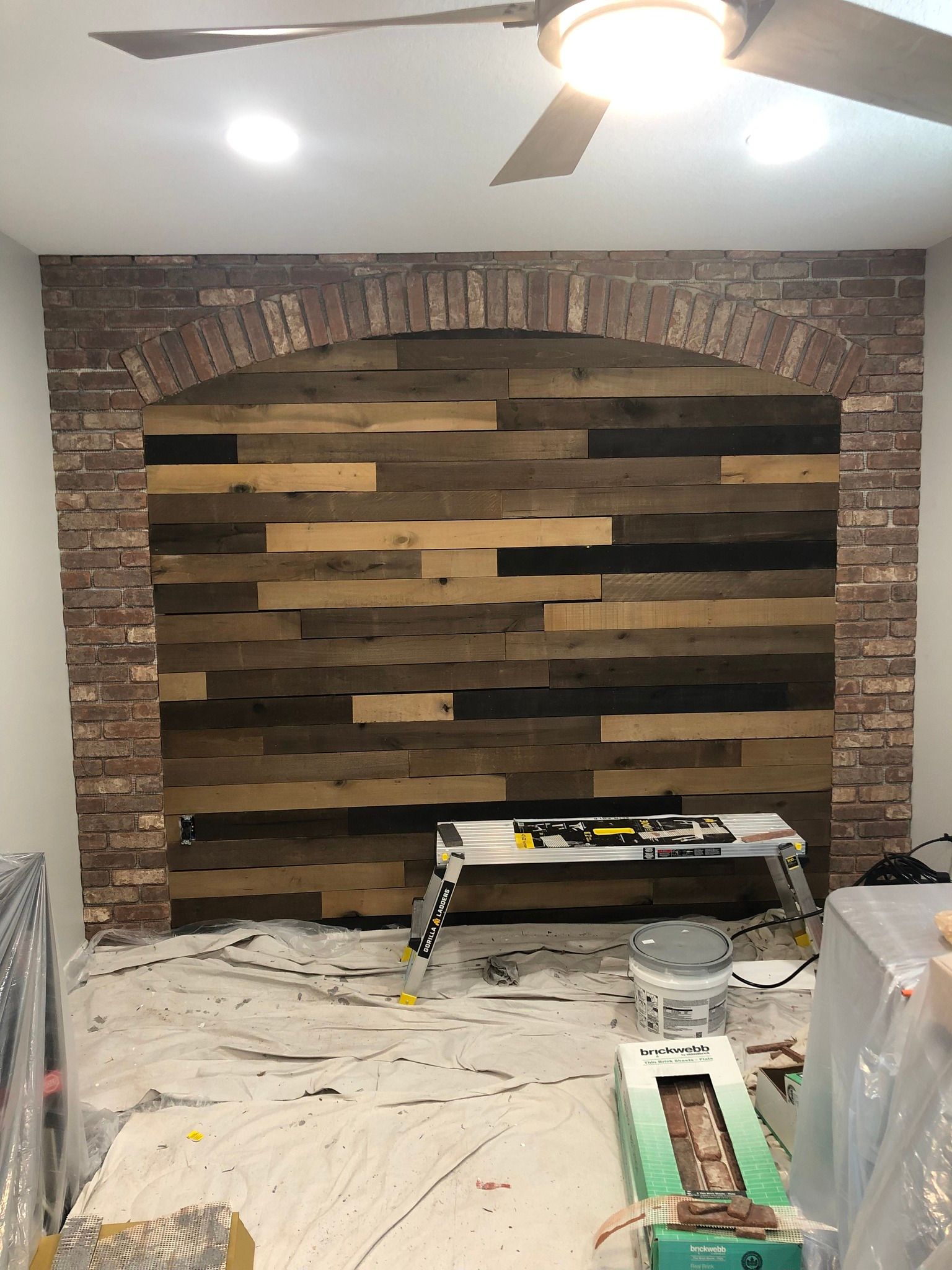 A modern kitchen with light grey wooden cabinets, stainless steel appliances, white countertops, and herringbone tile.