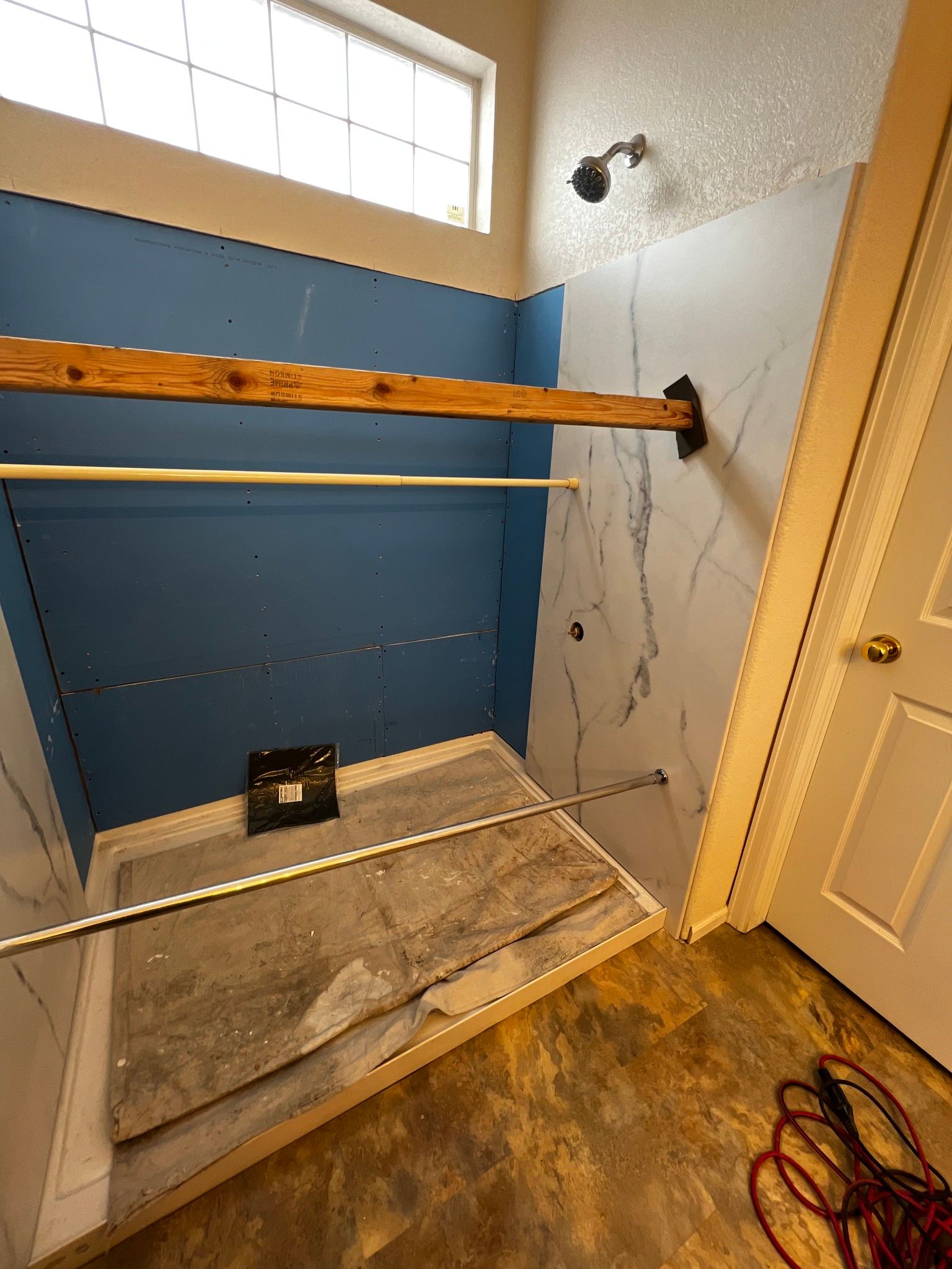 A bathroom shower under renovation with blue water-resistant drywall, partial marble-patterned paneling, and a shower base.