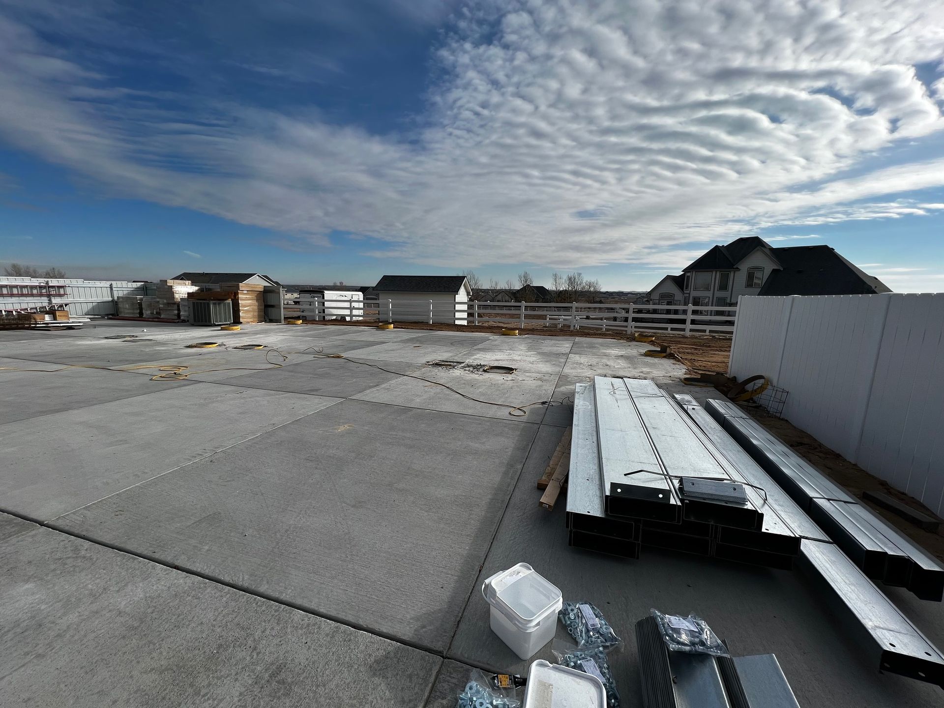 Construction site with a concrete slab, metal beams, and building materials under a cloudy sky.