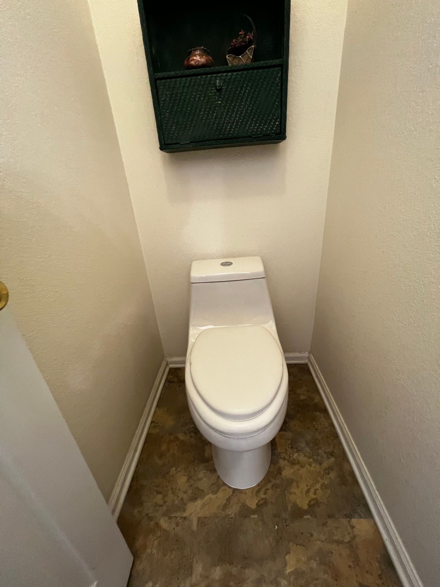 A white toilet in a small, enclosed bathroom with textured light-colored walls and mottled brown flooring.