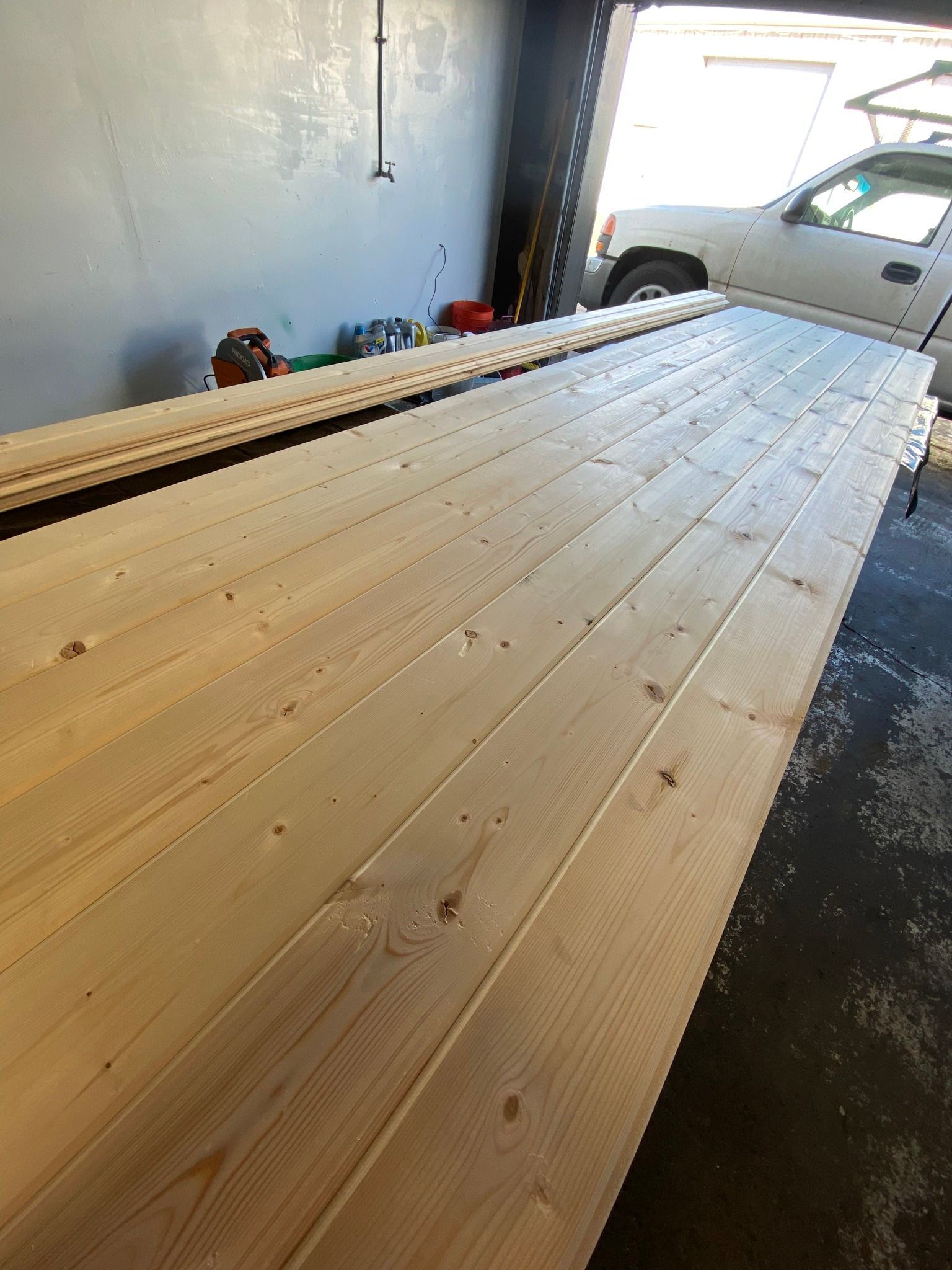 Several long, light-colored wooden planks laid side-by-side on a garage floor.