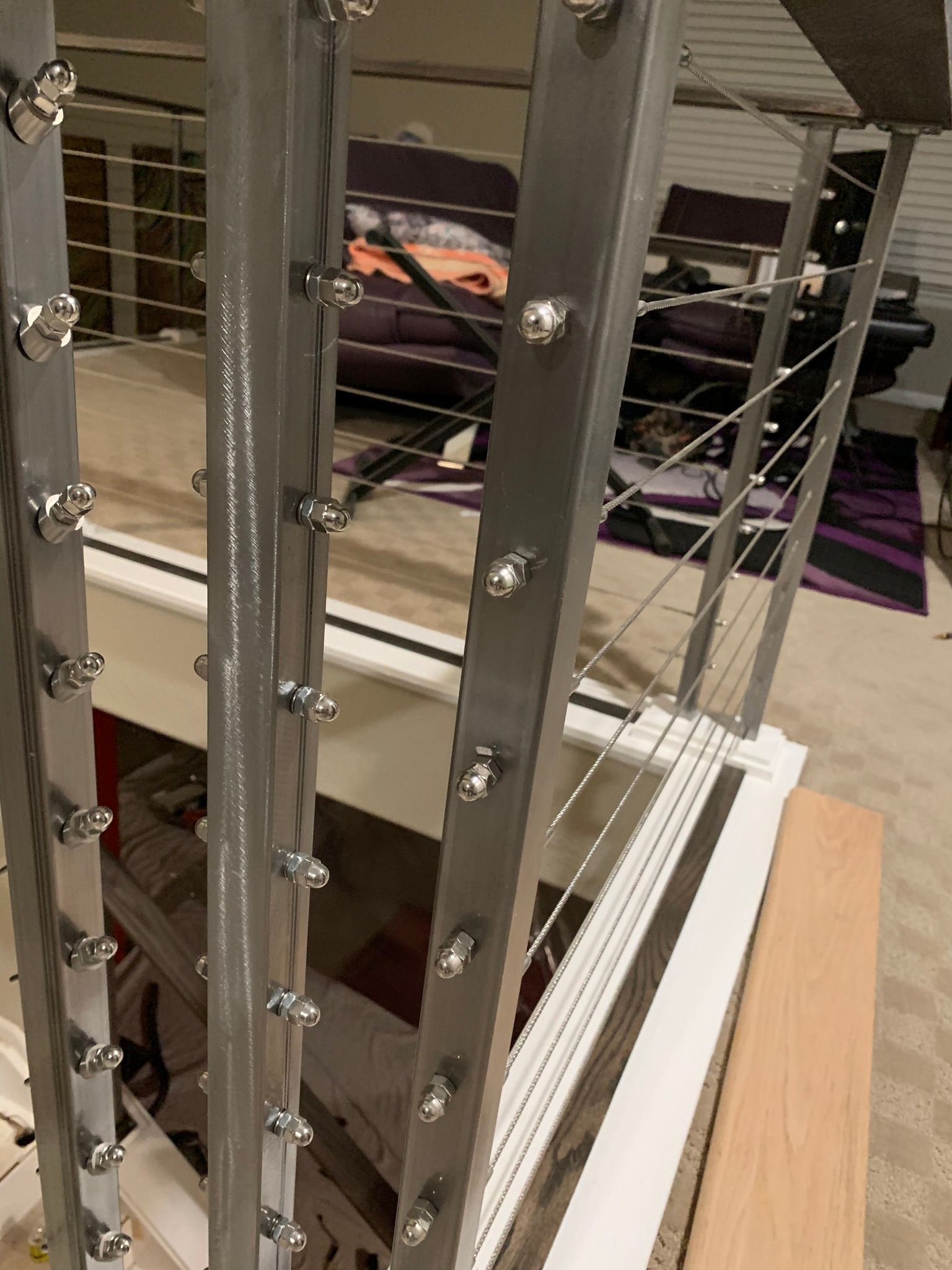 A close-up view of silver metal railing posts with horizontal cable tensioners installed on a staircase landing.