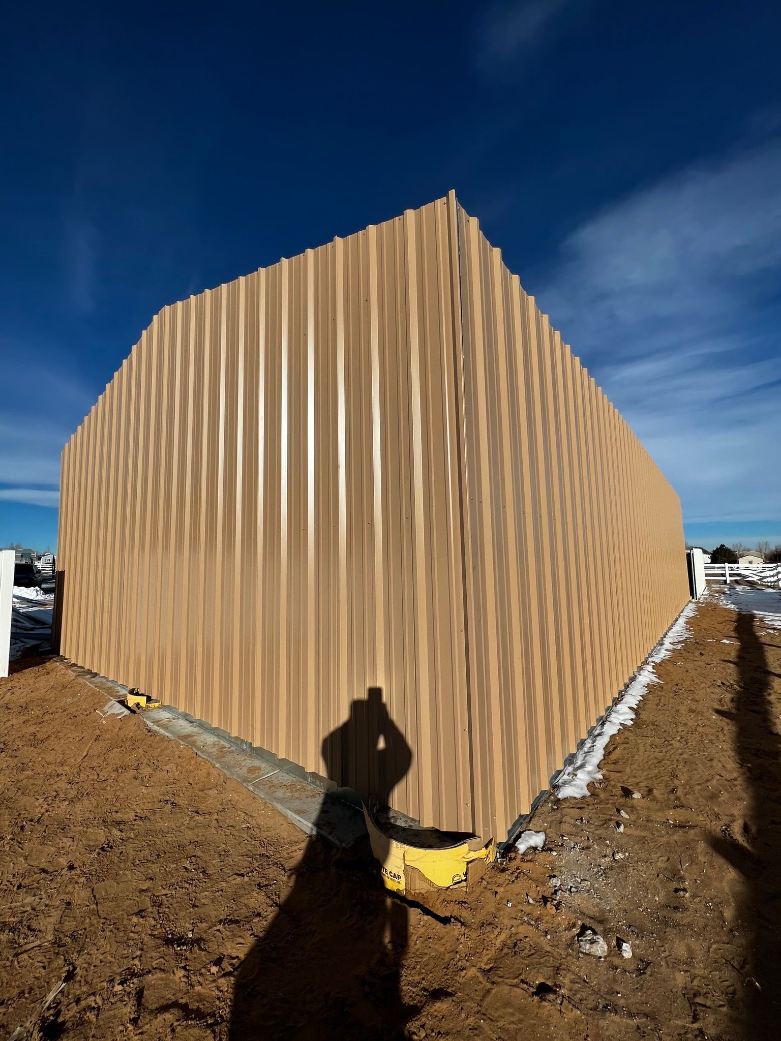 Exterior of a building under construction with tan, vertical-ribbed metal siding against a clear blue sky.