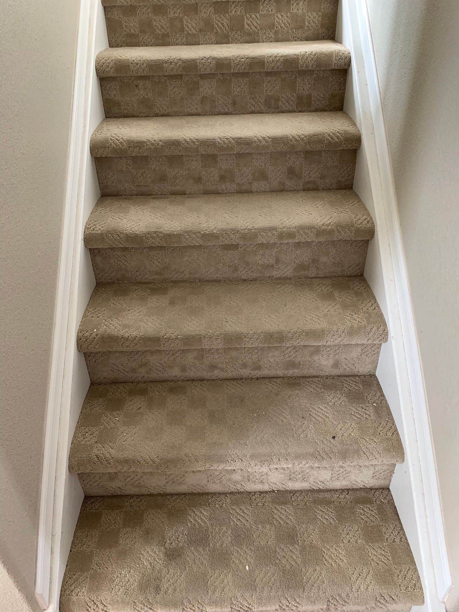 A set of indoor stairs covered in textured, beige patterned carpet between two white walls.