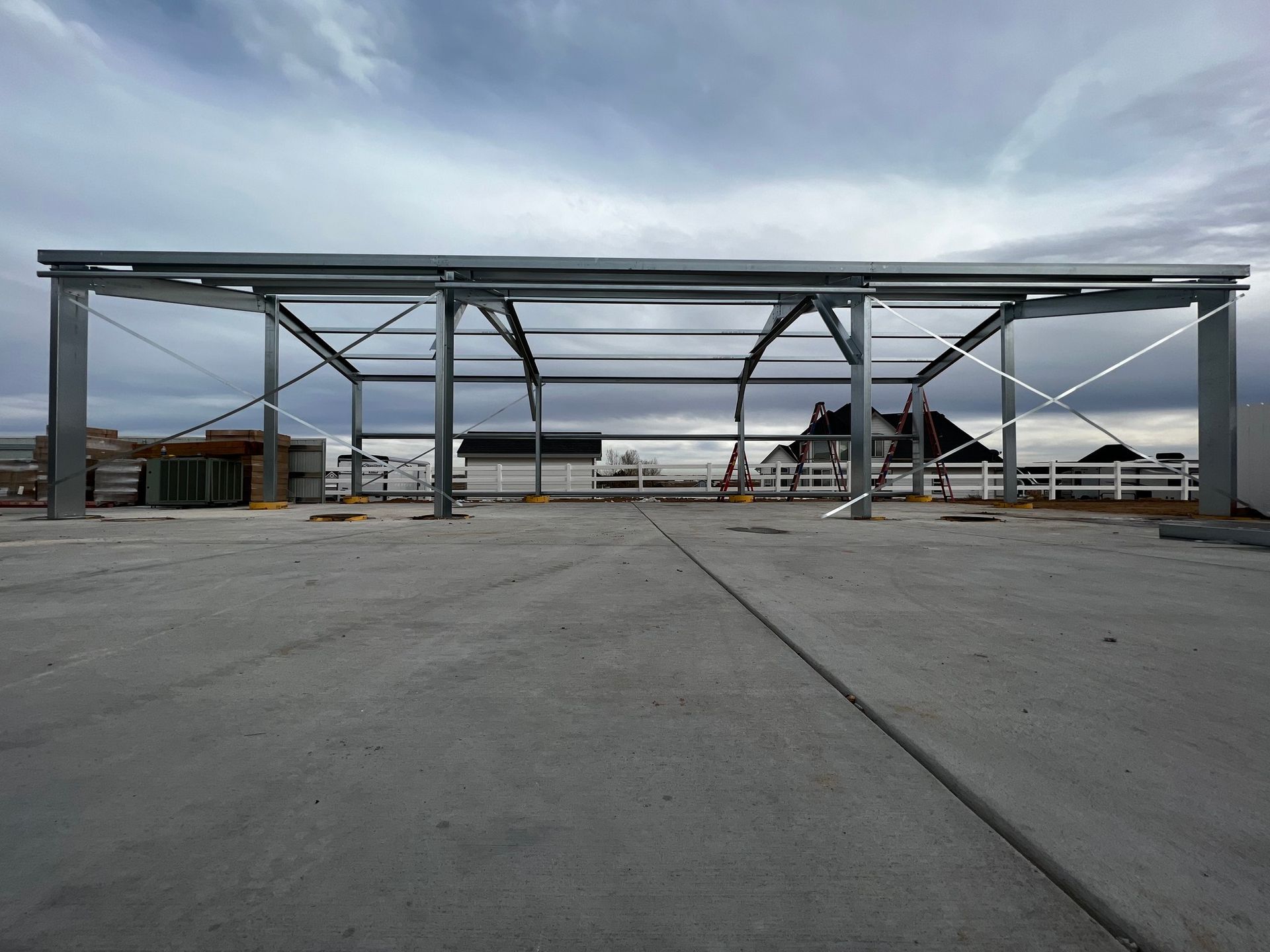 The metal frame of a building structure stands on a concrete foundation under a cloudy sky.